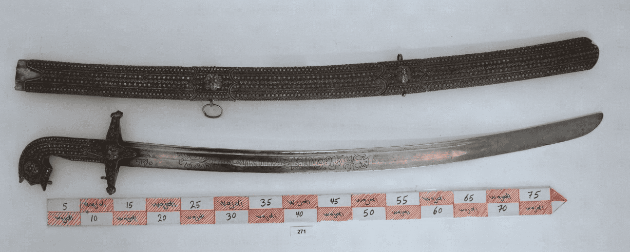 الوصف  : سيف مع الغمد مكون من النصل  والراس والغمد النصل عبارة عن صفيح قديم به خط محفور علية زخارف حديثة كتابات عربية وحروف مسند حديث الراس من المعدن المطرز بالمعدن على شكل منمنمات الغمد من المعدن المطرزبالمنمنمات?- المادة : حديد - معدن - الحقبة الزمنية   موروث